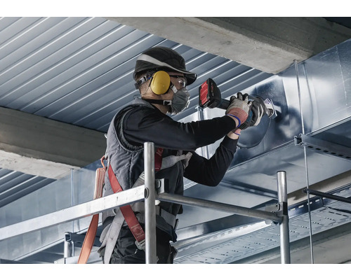 Un homme travaille sur un échafaudage avec une cintreuse de tubes sur un tuyau métallique.