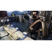 Un ouvrier répare des palettes en bois avec des outils dans un atelier.
