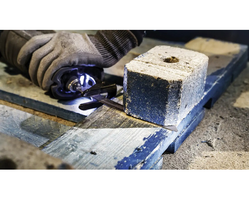 Une personne scie une briquette de charbon de bois sur une planche de bois avec une scie.