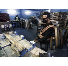 Un ouvrier répare une palette avec un cloueur pneumatique dans un hall d''usine.
