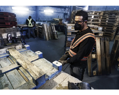Un ouvrier répare une palette avec un cloueur pneumatique dans un hall d''usine.