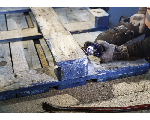 Une personne scie une palette en bois avec une scie sabre. Un pied-de-biche repose sur le sol.