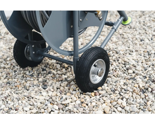 Gros plan d''un chariot à tuyau d''arrosage avec des pneus sur du gravier