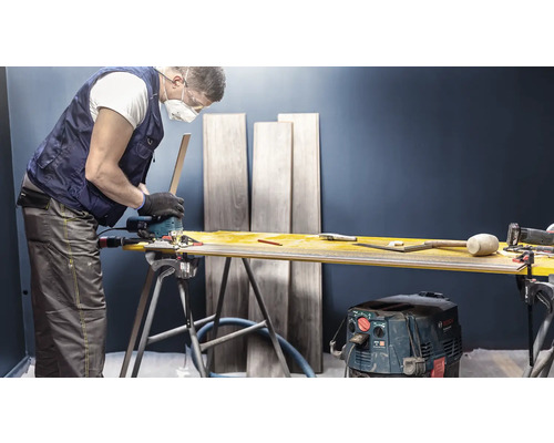 Un artisan coupe du stratifié avec une scie sauteuse sur un établi. Des planches de stratifié sont visibles à l''arrière-plan.