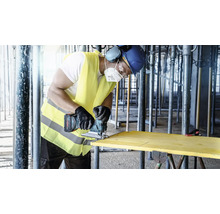 Un artisan scie une planche de bois avec une scie sauteuse sans fil sur un chantier.