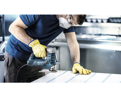 Un artisan portant un masque de protection, des lunettes de sécurité et des gants scie une pièce à l''aide d''une scie sauteuse.