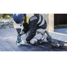 Ein Arbeiter verwendet ein Multifunktionswerkzeug auf einer Holzterrasse. Persönliche Schutzausrüstung ist ebenfalls vorhanden.