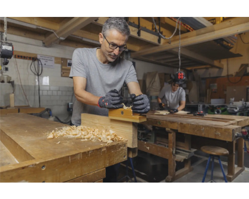 Un homme rabote du bois sur un établi dans un atelier.