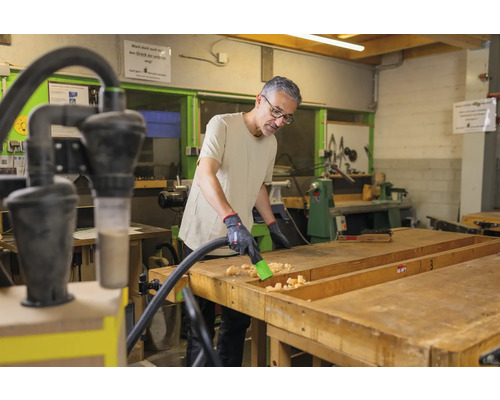 Un homme nettoie un établi avec un aspirateur dans un atelier.