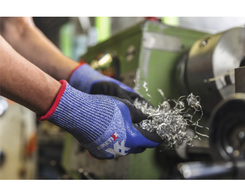 Des mains portant des gants de protection tiennent des copeaux de métal devant un tour