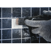 Handwerker mit Multifunktionswerkzeug entfernt eine Fliese.
