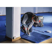 Artisan coupant de la moquette avec un outil spécial, aspirateur industriel en arrière-plan