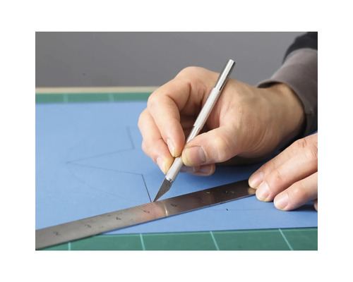 Person schneidet mit Skalpell und Lineal Papier