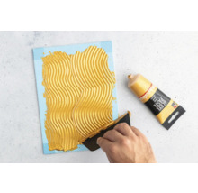 Application de pâte structurante sur une toile à l''aide d''un couteau à mastic à côté d''un tube de pâte structurante.