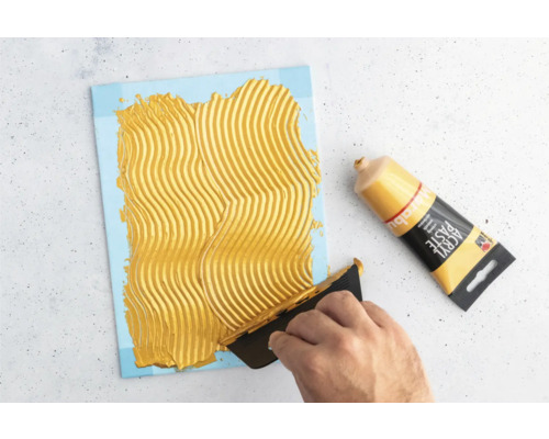 Application de pâte structurante sur une toile à l''aide d''un couteau à mastic à côté d''un tube de pâte structurante.