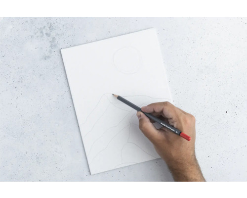 Main dessinant au crayon un paysage de montagne sur une feuille de papier blanche