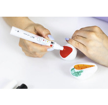 Eine Person bemalt einen Stein mit einem roten Stift, während ein weiterer Stein mit einer Karotte im Vordergrund liegt.