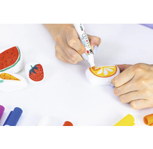 Eine Person bemalt Steine mit Motiven von Wassermelone, Erdbeere, Karotte und Orange mit einem Farbstift.