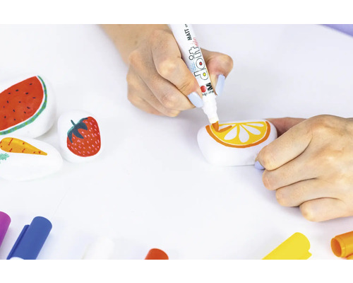 Eine Person bemalt Steine mit Motiven von Wassermelone, Erdbeere, Karotte und Orange mit einem Farbstift.