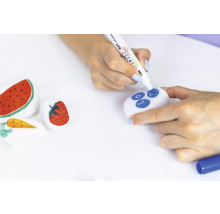 Bemalte Steine mit Obstmotiven und eine Person, die einen Stein mit einem Stift bemalt.