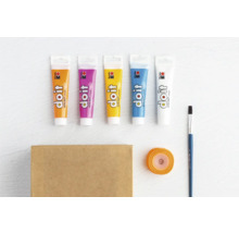 Verschiedene Tuben Farbe, Pinsel, Geschenkband und ein Karton liegen auf einem Tisch.