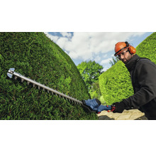 Une personne taille une haie avec un taille-haie.