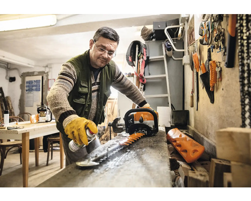 Un homme nettoie la lame d''un taille-haie avec un spray dans un atelier.