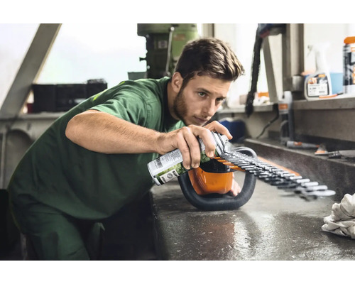 Un homme vaporise un spray d''entretien sur un taille-haie pour entretenir les lames.