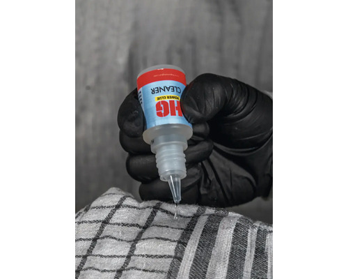 Une main gantée tient un nettoyant HIG Power Glue qui laisse tomber une goutte.