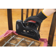 Eine Hand mit Handschuh verwendet einen Tacker, um einen Stuhl neu zu beziehen.