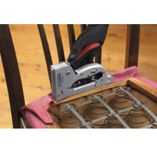 Eine Hand mit Handschuh befestigt Stoff mit einem Handtacker auf einem Stuhl.