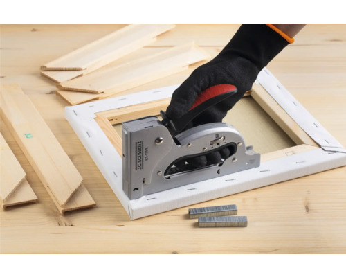 Hand mit Handschuh benutzt einen Handtacker an einer Leinwand