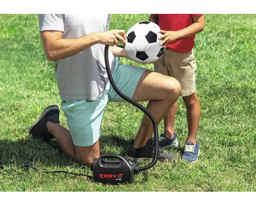 Eine Person pumpt einen Fussball mit einer elektrischen Luftpumpe auf dem Rasen auf.