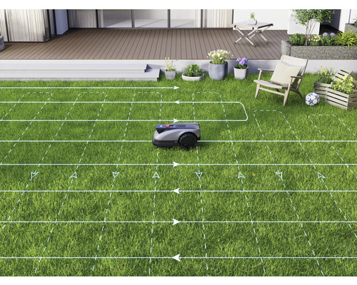 Une tondeuse à gazon robotisée tond une pelouse dans un jardin avec une terrasse.