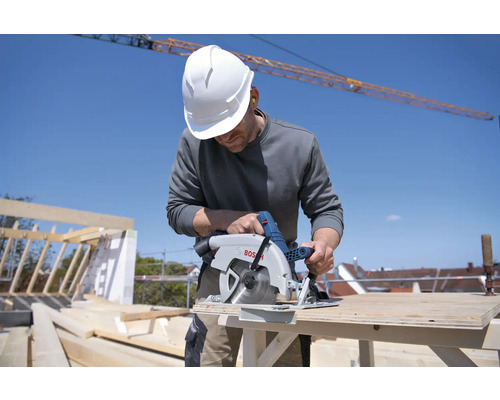 Handwerker mit Schutzhelm sägt Holz mit einer Bosch Kreissäge auf einer Baustelle.