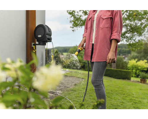 Frau giesst Pflanzen mit einem Gartenschlauchsystem von der Wand