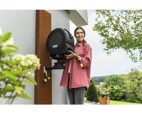 Frau hält eine automatische Kärcher-Gartenschlauchbox an der Wand