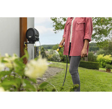 Une femme utilise un dévidoir Kärcher pour arroser le jardin.