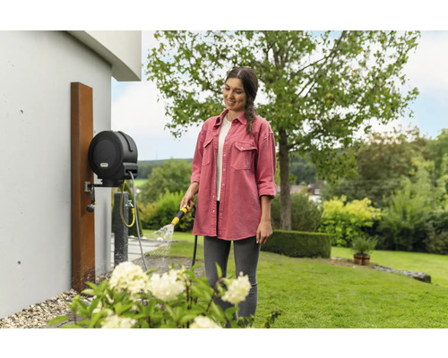Frau giesst Blumen mit einer Kärcher Schlauchbox in einem Garten.