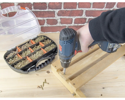 Eine Person arbeitet mit einem Akkuschrauber an einem Holzrahmen, Schrauben und ein Schraubensortiment sind im Bild zu sehen.