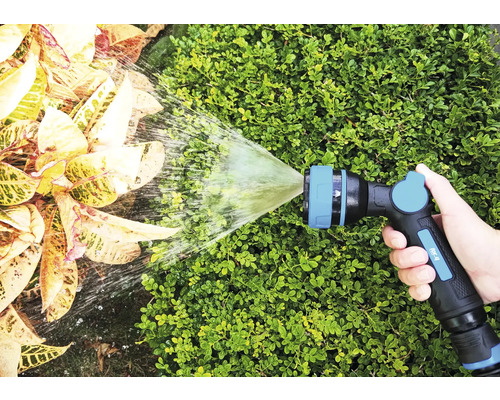 Une main tient un pulvérisateur de jardin qui arrose les plantes.