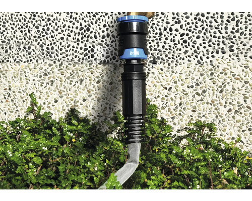 Raccord de tuyau d''arrosage devant un mur et des buissons