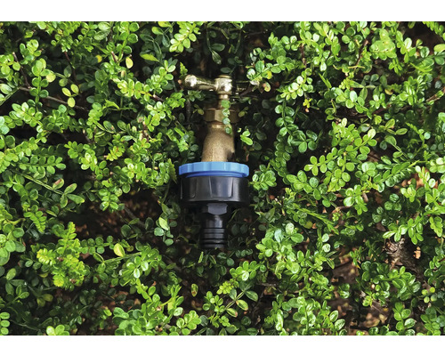 Raccord de tuyau d''arrosage devant des feuilles vertes