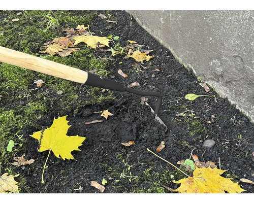 Gros plan d''une houe avec manche en bois dans la terre du jardin.