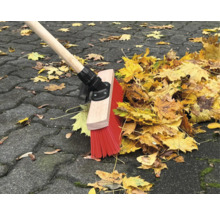 Une balayeuse avec un manche en bois et des poils rouges balaie les feuilles sur une chaussée.