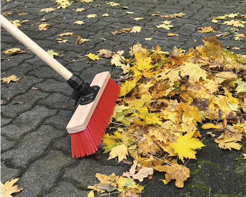 Besen kehrt Herbstlaub auf Pflastersteinen zusammen