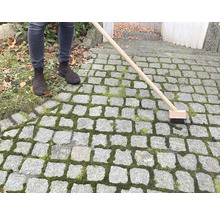 Person reinigt Steinpflaster mit Fugenbürste
