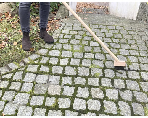 Personne nettoyant le pavé en pierre avec une brosse à joints