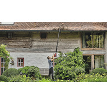 Un homme nettoie une gouttière avec un nettoyeur de gouttière devant une maison.