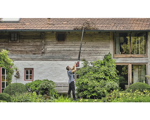 Un homme nettoie une gouttière avec un nettoyeur de gouttière devant une maison.